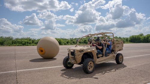  People riding in an all-terrain buggy next to a large ball. 